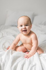 Smiling newborn baby on a white bed at home, the concept of a happy healthy infant baby. Generation alpha and gen alpha