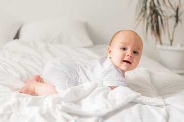 Smiling newborn baby on a white bed at home, the concept of a happy healthy infant baby. Generation alpha and gen alpha