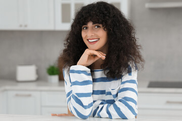 Fototapeta na wymiar Portrait of beautiful woman with curly hair in kitchen. Attractive lady smiling and looking into camera
