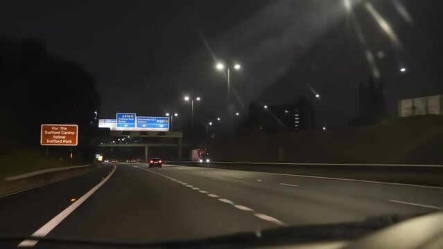 Blurry car dashboard and windshield view driving M602 highway at night in Salford, Greater Manchester, United Kingdom.