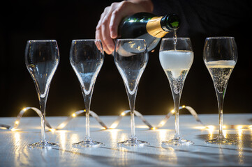 New year party, pouring of brut champagne bubbles cava or prosecco wine in tulip glasses with garland  lights on background