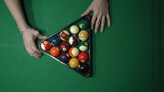 Close up man with plastic triangle rack with billiard balls on green table indoors