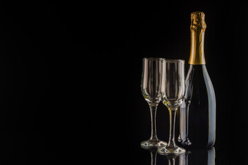 Champagne bottle and two champagne glasses on black background with copy space. New Year and Christmas celebration concept.