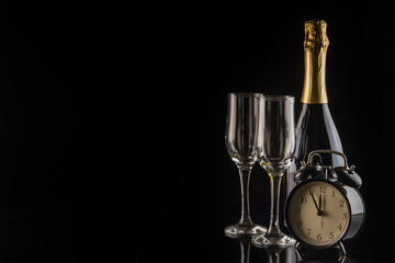 Alarm clock, champagne bottle and glasses on black background with copy space. New Year and Christmas celebration concept.