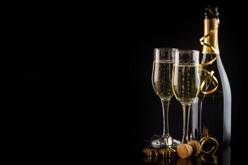Two glasses of champagne, candles and a bottle on a black background. New Year and Christmas celebration concept.