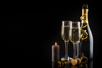 Two glasses of champagne, candles and a bottle on a black background. New Year and Christmas celebration concept.