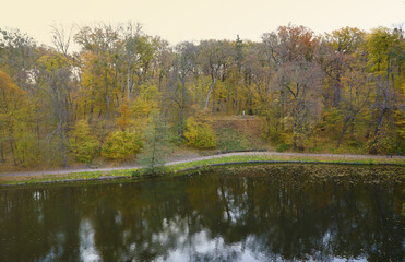 Beautiful Nature Autumn landscape with lake. Scenery view on autumn city park with golden yellow foliage in cloudy day. Walking paths in the city Park strewn with autumn fallen leaves