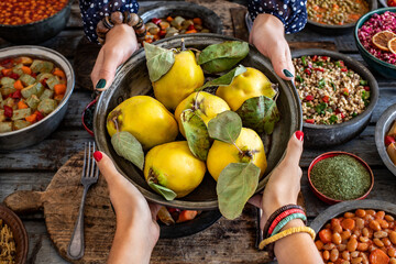 Fresh and ripe quinces a the hand of two women in the copper bowl. Many types of vegan foods on the table with fruits. 