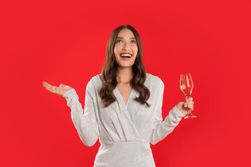 woman elegantly celebrates with glass of sparkling wine, red background