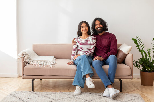 Happy millennial indian couple sitting on couch in living room