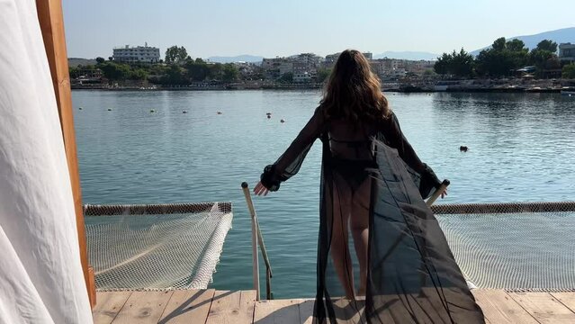 a beautiful girl in a black pareo enters the water in Albania along a wooden bridge VIP place Go swimming wet your feet rest hammocks wonderful relaxation travel. go down the steps to the water