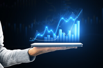 Hand holding tablet displaying growth charts and stock market trends