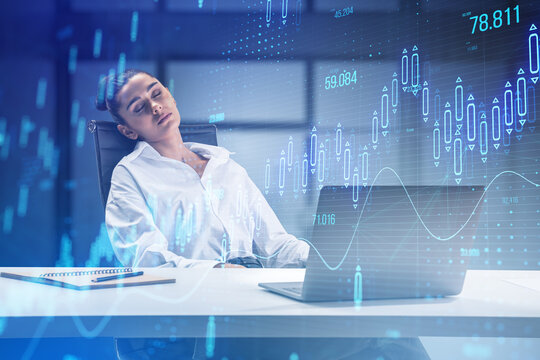 Attractive sleepy businesswoman at desk with glowing candlestick forex chart on blurry office interior background. Stock market and investment concept. Toned image. Double exposure.
