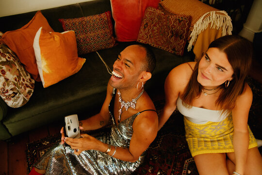 Young non-binary person of Caribbean mixed race laughing with their white female friend holding a vintage disposable camera