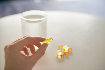 Close up of woman hand taking yellow capsule of omega 3, 6, 9 vitamins and D . Winter health care concept. Selective focus natural light photo.
