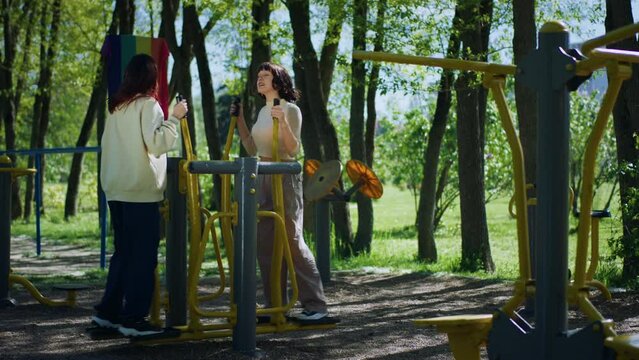 Attractive young ladies practice outdoor gym in the middle of the park using public sport equipment