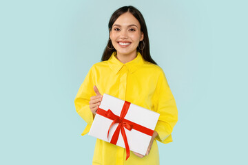 Positive young woman holding gift box and smiling