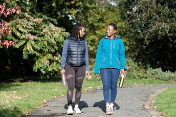 Two mature women friends smiling and walking on a park path.