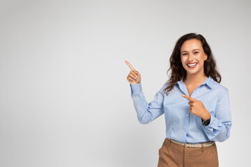 Glad young european businesswoman in formal wear pointing fingers at empty space