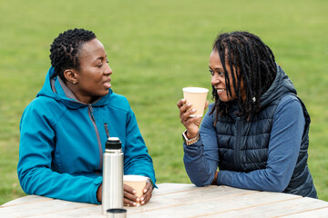 Two mature black women having coffee on table outdoors.