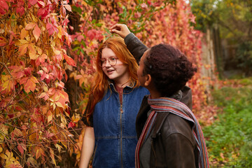 Young girl removing leaf from her friend's red hair. Concept of gender-neutral and sustainable fashion and self expression