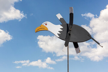 Wooden seagull wind vane with rotation wings.. Nice blue sky with fluffy white clouds.