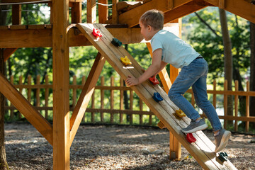 A little boy doing climbing exercises on a wooden playground