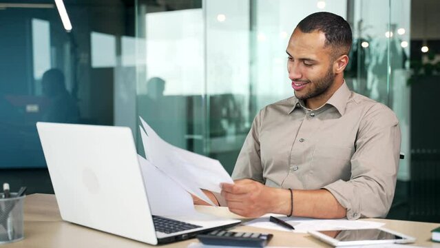 Happy male businessman financier is satisfied looking at documents data analysis or company read financial report while sitting in office at workplace at computer desk. entrepreneur employer growth