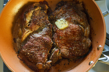 Beef steak, golden-browned and searing in a hot frying pan on the stove
