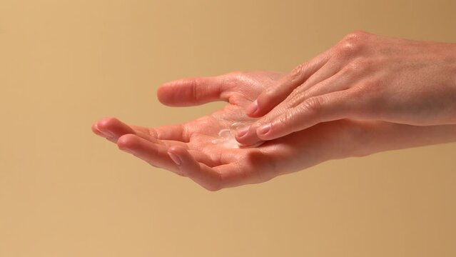 Woman applies cream on palm with finger and rubs it on beige isolated background. Body and face skin care concept, cosmetic texture