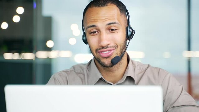 Customer service and telemarketing male agent in office doing computer consultation with headset. Positive latin handsome black man call center consultant operator working on crm online in workplace 