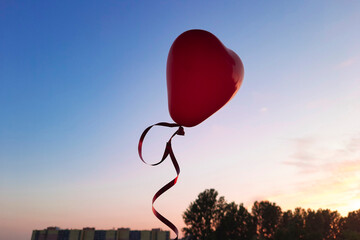 Red heart shaped balloon flies against the background of the sunset sky. Concept for romantic,...