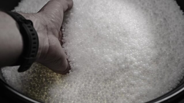 A factory worker checks plastic pellets before they are put into production. White compound in a man's hand. Production