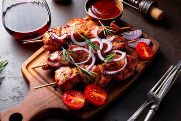 Pork kebab with barbecue sauce and tomatoes and a glass of red wine on a dark table close up