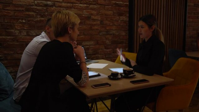 Three young business colleagues having a meeting in a modern cafe in the late evening hours. Successfull team brainstorming after work hours..
