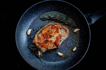 Chef cooking juicy beef meat on frying pan with rosemary and garlic, uses kitchen utensils. Process of roasted steak cooking.