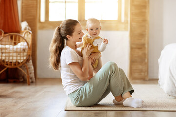 Cheerful Young Mom Holding Baby In Arms Smiling
