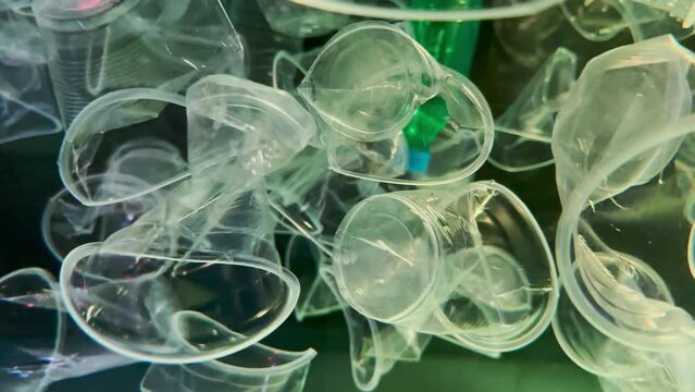Close-up of plastic debris floating under surface in blue water, Slow motion. Disposable plastic cups and other trash littering oceans of planet