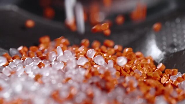 Macro frame of white and orange plastic granules. The polymer composite is poured into a tank for further production and casting in special molds. Production