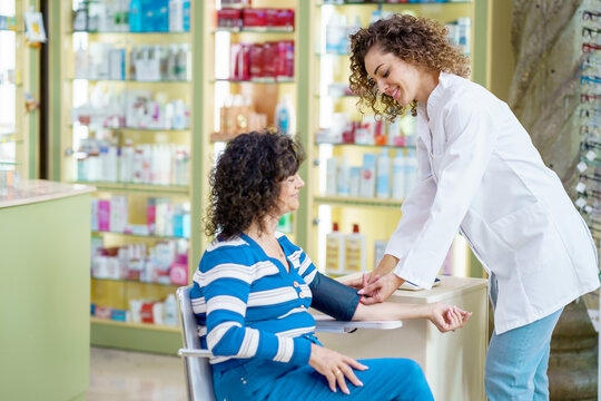 Happy young woman pharmacist checking blood pressure of lady customer in pharmacy