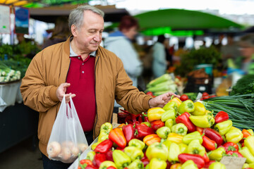  eElderly man buys vegetables at an open-air market