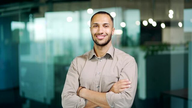 Portrait of a happy young arab latino specialist standing in a modern office. Handsome latin african american man looks at the camera Sincere smiling successful Male entrepreneur at workplace indoors