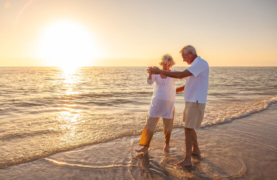 Happy Senior Old Retired Couple Walking Dancing Holding Hands on Beach at Sunset