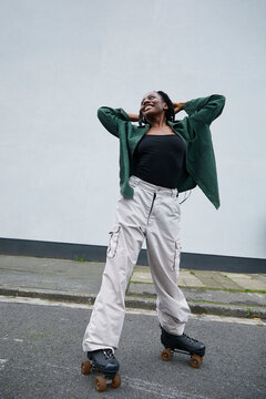 Smiling black woman with long braids and stylish outfit posing in her rollerskates outdoors