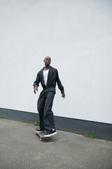 Stylish Gen Z black boy with blonde hair skating on sidewalk whilst wearing black jumpsuit © Ejatu Shaw