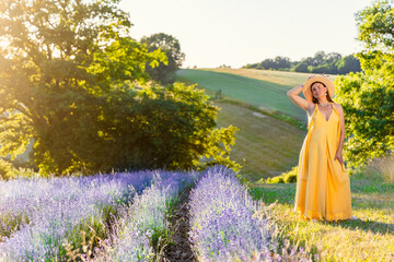 A pregnant woman in a yellow dress stands on the edge of a field of blooming lavender in the rays...
