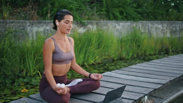 Tranquil yogini meditating tablet on park bench. Woman lotus pose watching tab
