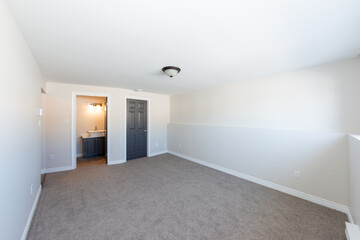 An empty master bedroom with a white ceiling, beige painted walls and grey carpet in a house....