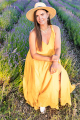 A pregnant woman in a yellow dress sits on a blooming lavender field