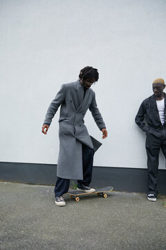 Gen Z black boy with locs standing on skateboard on sidewalk with his friend